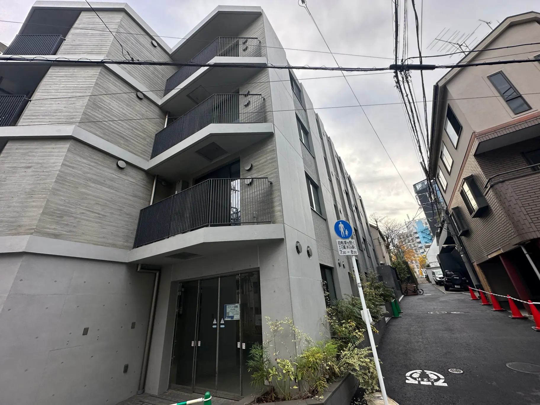 近代的な外観のアパートメントビル、歩道標識と植栽がある都市の狭い通り
