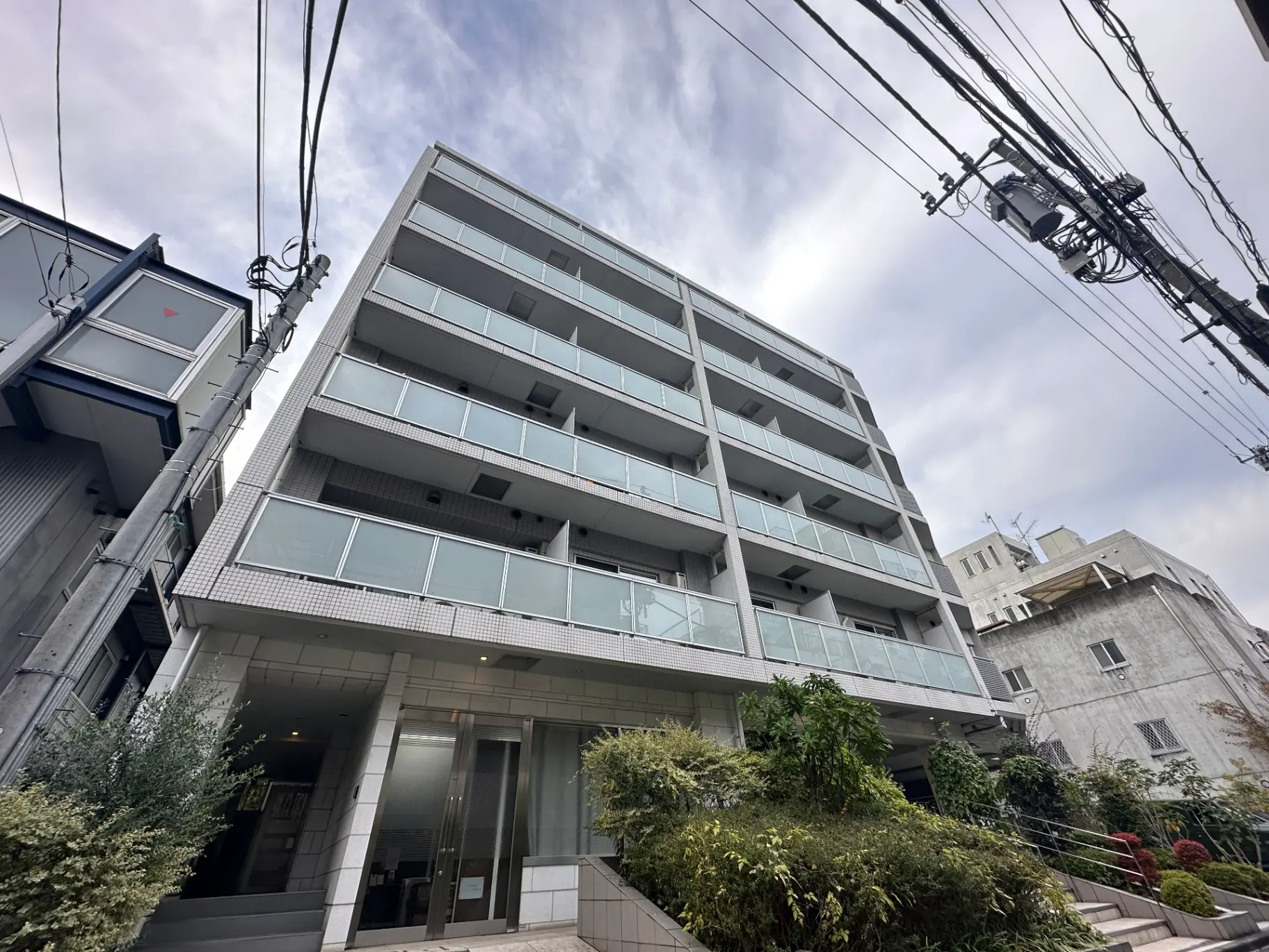 都市の住宅街にある現代的なマンションの外観、曇り空の下でバルコニーと入り口が見える