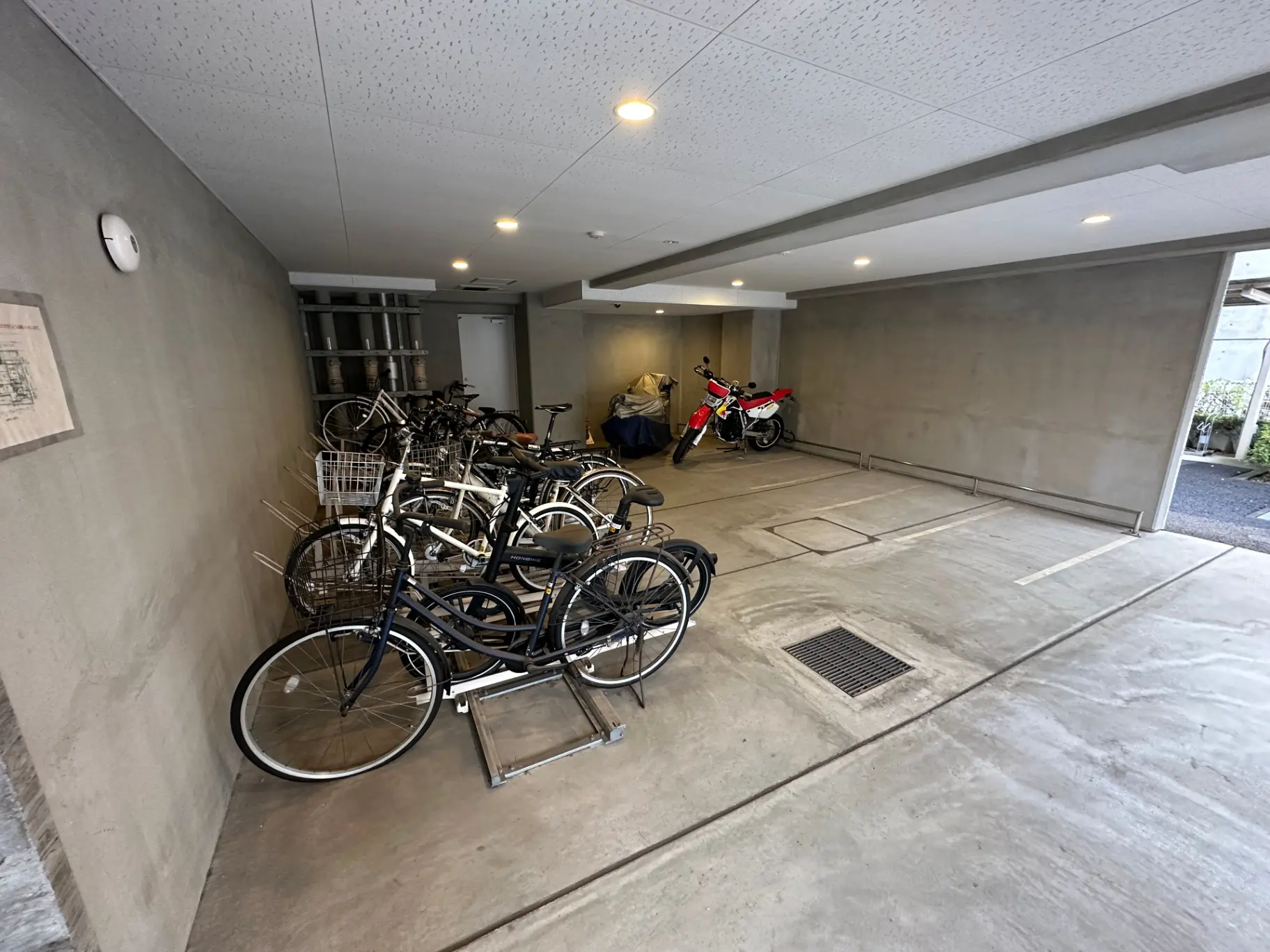 室内駐輪場に並ぶ自転車とバイク、コンクリートの床と白い壁のあるシンプルなデザイン