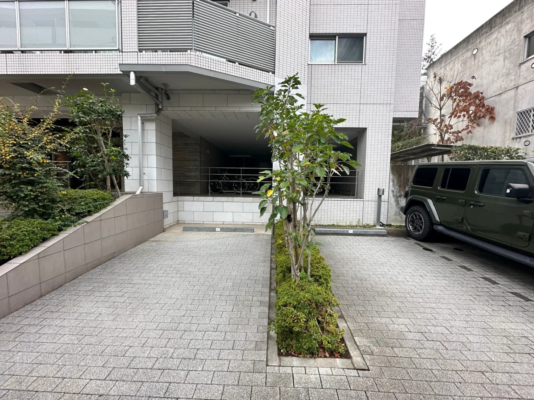 都市のモダンな建物のエントランス、緑の植栽と駐車している緑色のSUV車