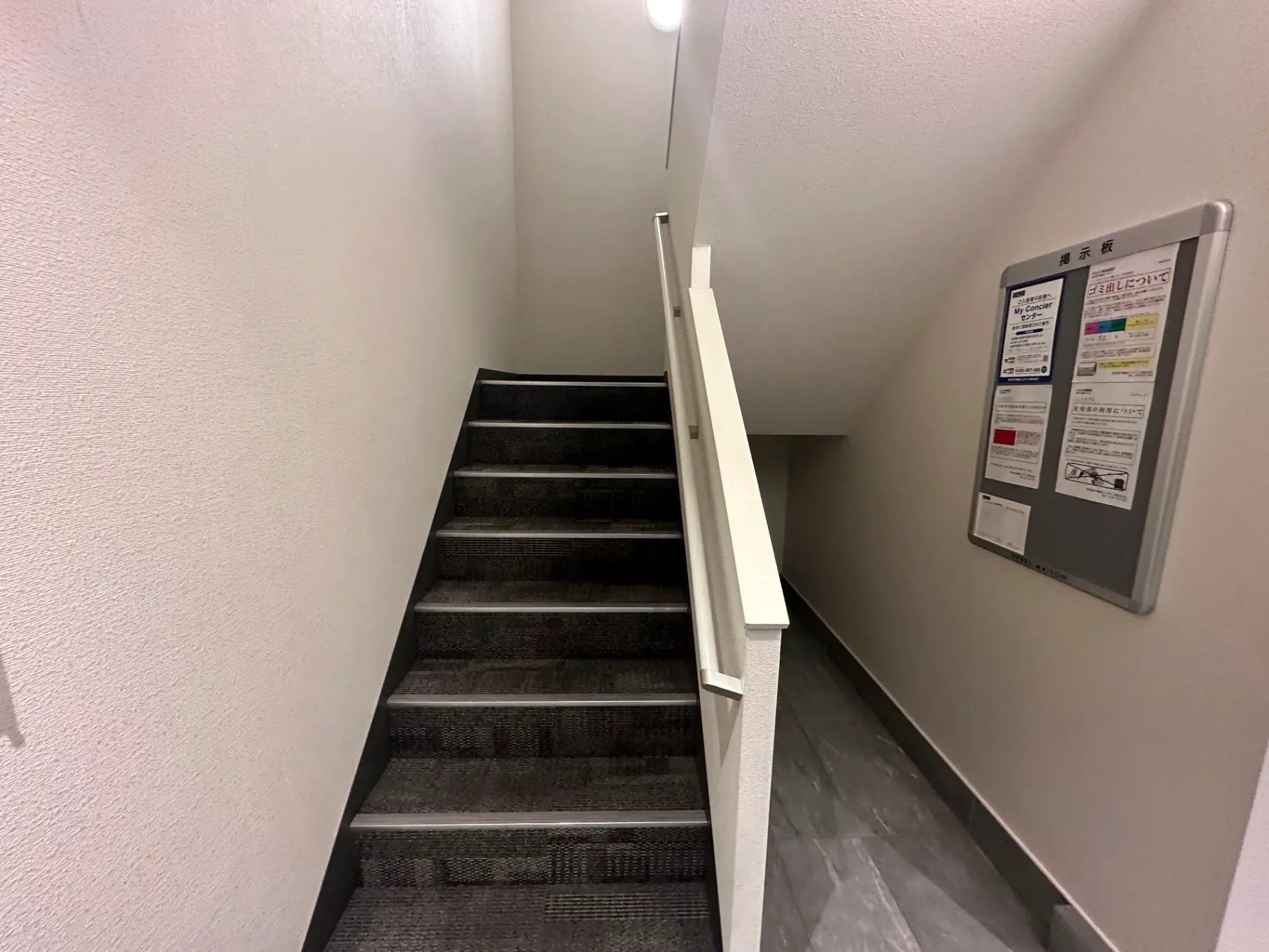 建物の階段と掲示板、白い壁とグレーのカーペットがあるシンプルなデザインの室内