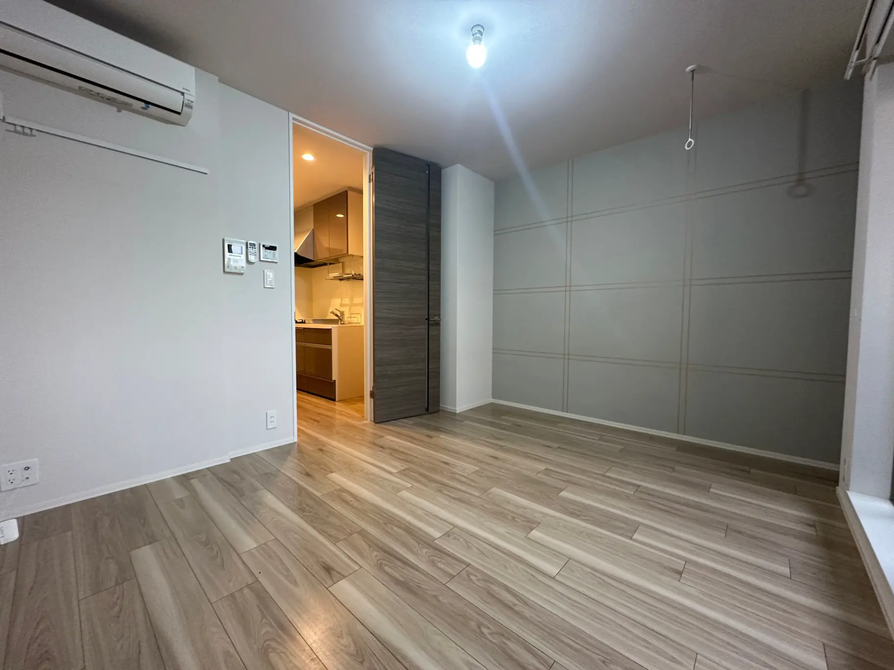 シンプルなデザインの新築マンションの空き部屋、木目調フローリング、キッチンへの開口部、天井の照明