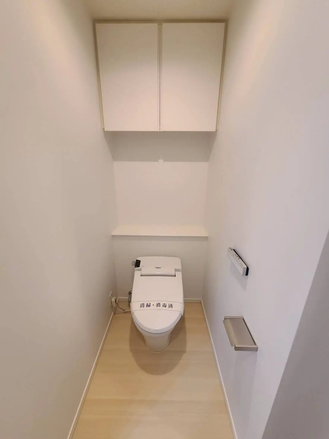 シンプルなデザインのトイレルーム、洗練された白い壁と木製フローリング、ウォシュレット付きトイレット設備