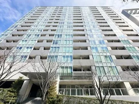 現代的なデザインの高層マンション、ガラス張りの外観と周囲に並ぶ樹木、青空が広がる風景