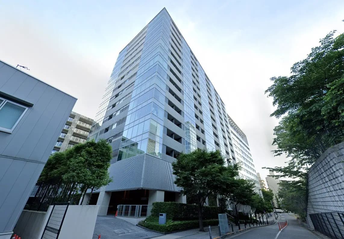 - モダンなガラス張りの高層マンションの外観、緑豊かな植栽と広々としたエントランス周辺の風景