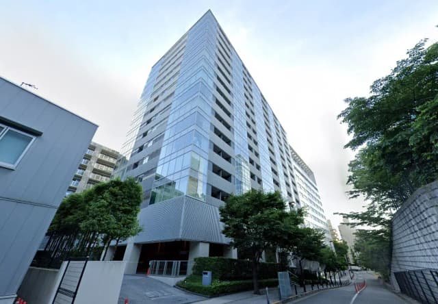 - モダンなガラス張りの高層マンションの外観、緑豊かな植栽と広々としたエントランス周辺の風景