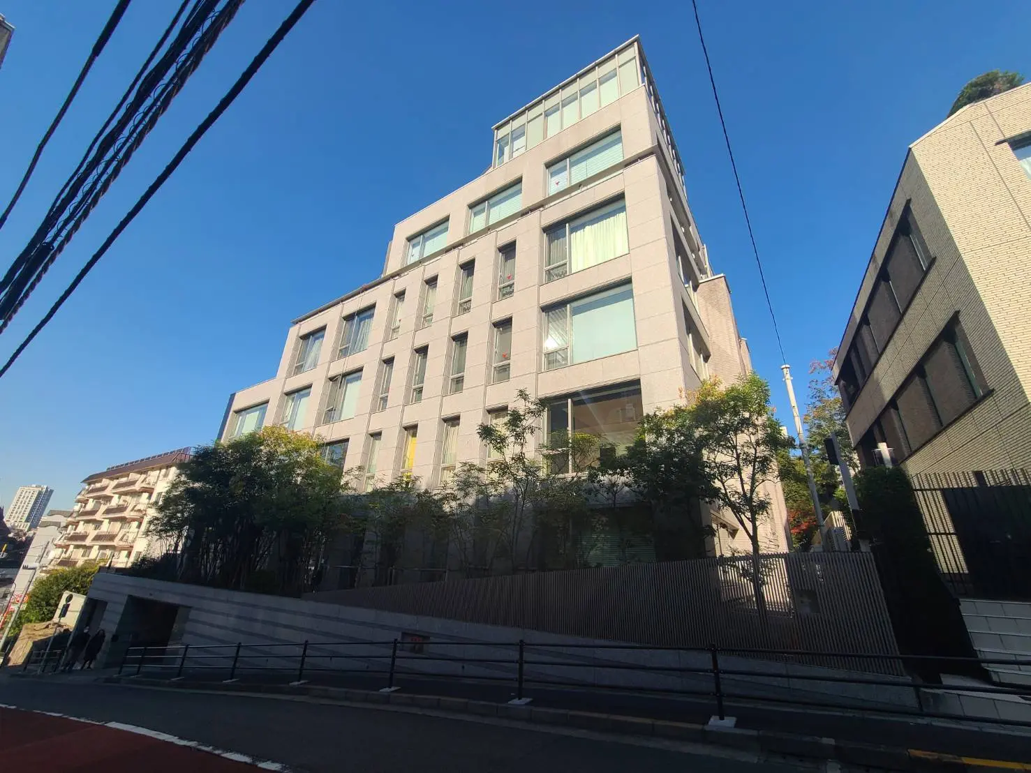 清潔でモダンな外観のオフィスビル、青空と電線、周囲に住宅エリアが見える街並み