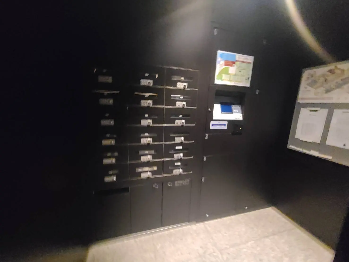 暗い廊下に設置された郵便受けと自動販売機、掲示板のあるマンション内の共有スペース