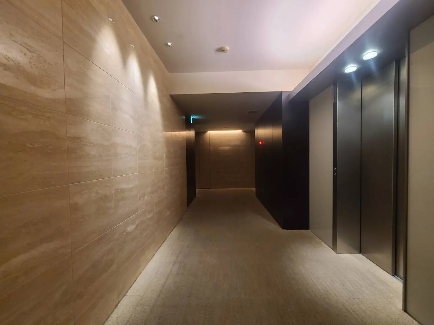 モダンな建物の廊下、ベージュの壁タイル、絨毯敷きの床、LED照明が備えられた清潔感のあるインテリア