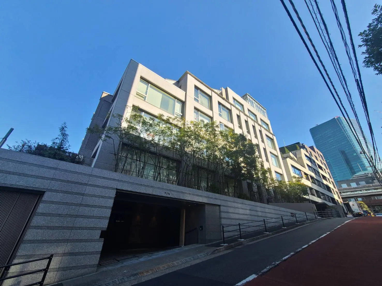 都市のモダンなオフィスビル、クリアな青空と緑豊かな植栽、ガラス窓が特徴的な建築デザイン