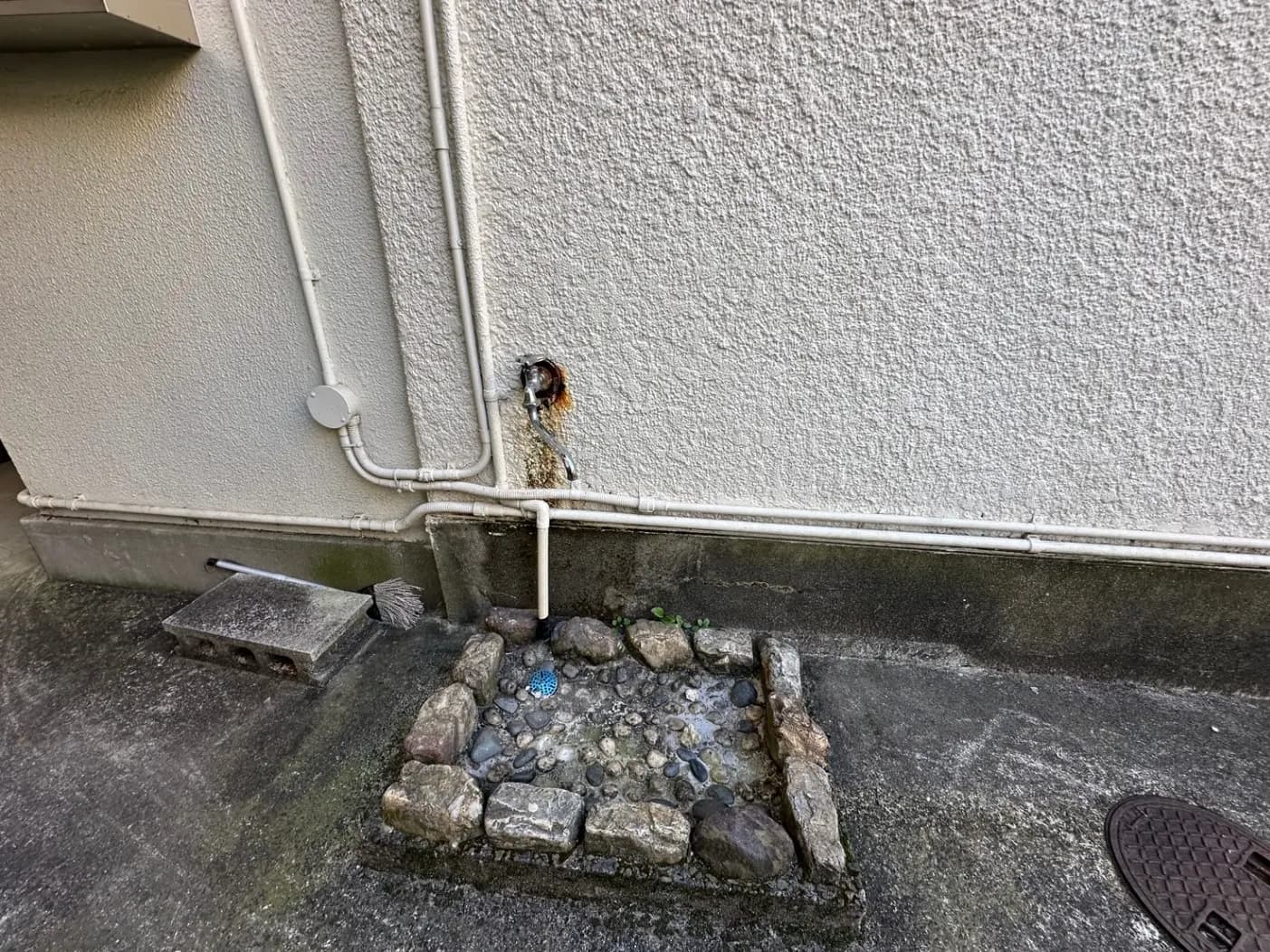 家の外壁と排水溝、石と小道具が敷かれた水回り