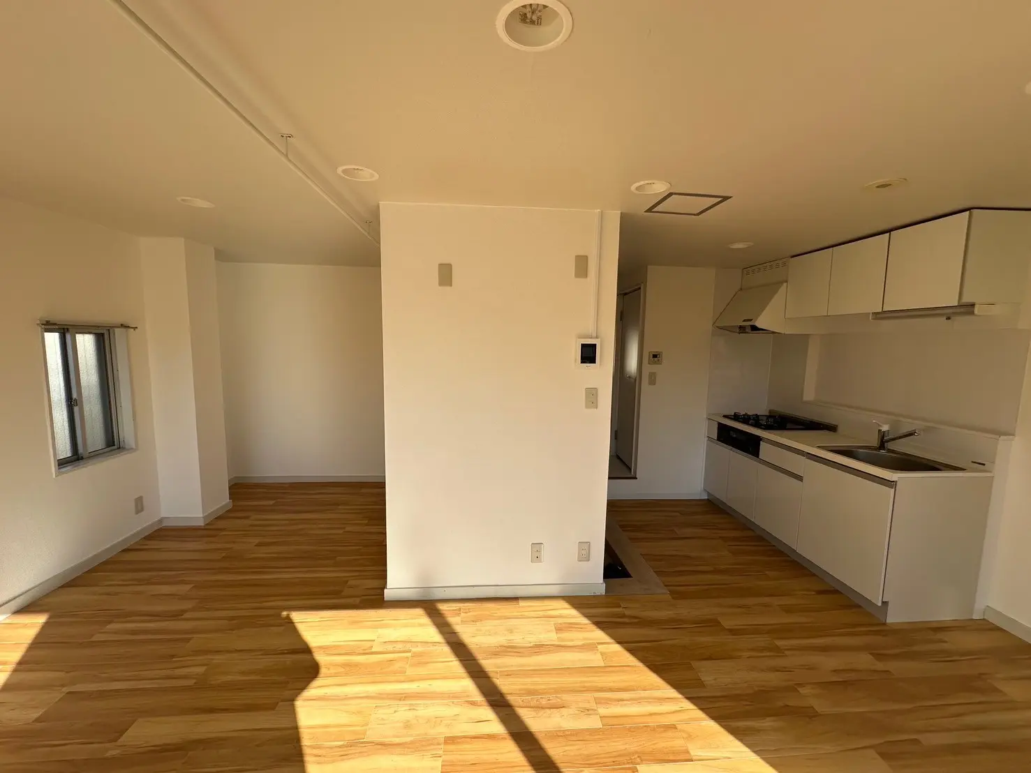 明るい自然光が差し込む新築マンションのキッチン付きリビング、無垢材フローリング、モダンな白いキャビネット
