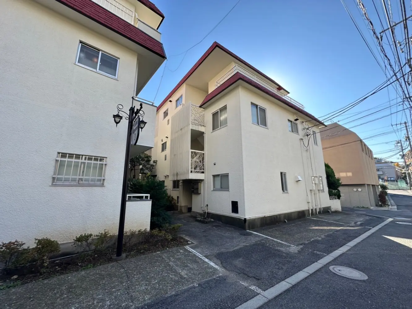 日本の住宅街にあるアパートの外観、青空と共に照らされた建物、駐車スペースあり