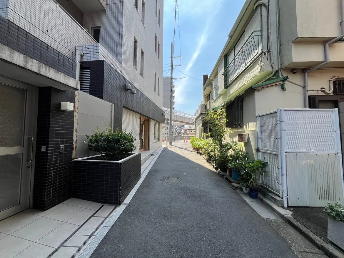 - 都市の静かな裏路地、両側に植栽が並び、黒いタイルの建物と古い建物が対比する風景