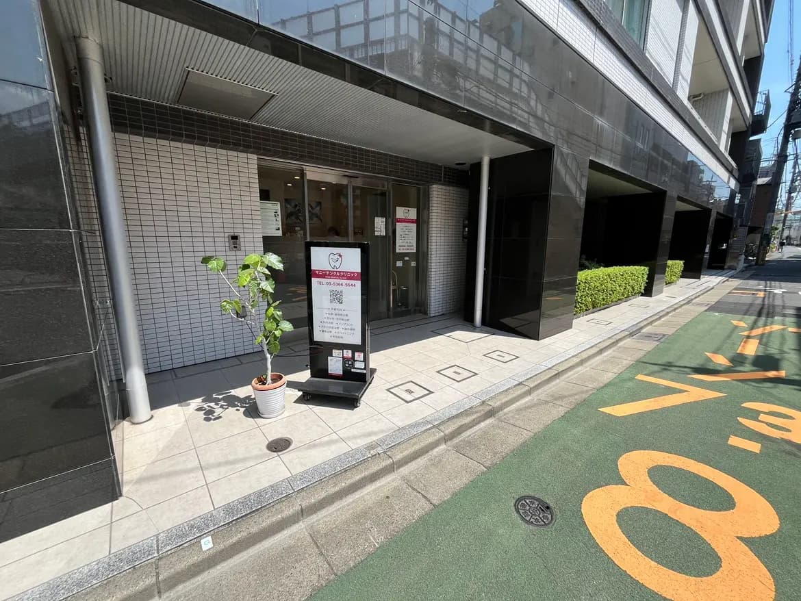 - 現代的な歯医者のエントランス、ガラスの扉と案内看板、テラスには観葉植物が配置された外観