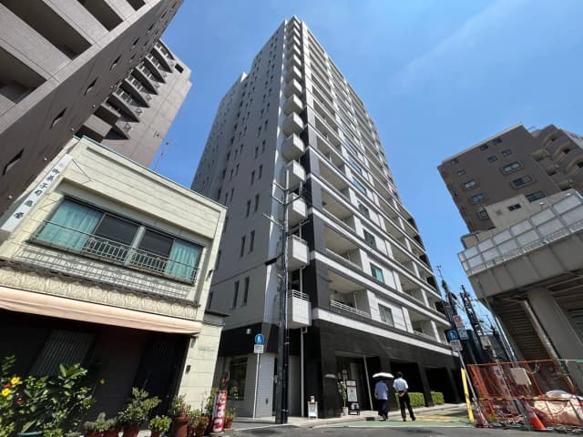 - 高層マンションと古い建物が共存する街並み、青い空に映える建物のファサード、通りを歩く人々の姿