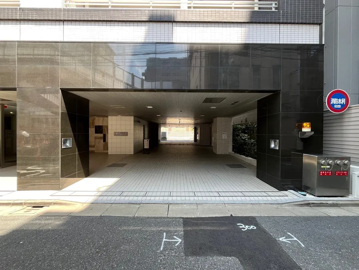 - 都市のエントランス、暗い石材の壁とタイル張りの床、奥に続く明るい通路が見える風景