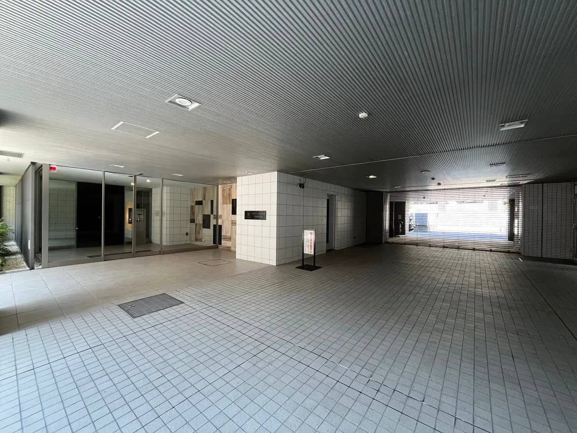- モダンな建物のエントランス、広々としたロビーに明るい照明と開放的なガラス扉、タイル張りの床が特徴的な内部空間