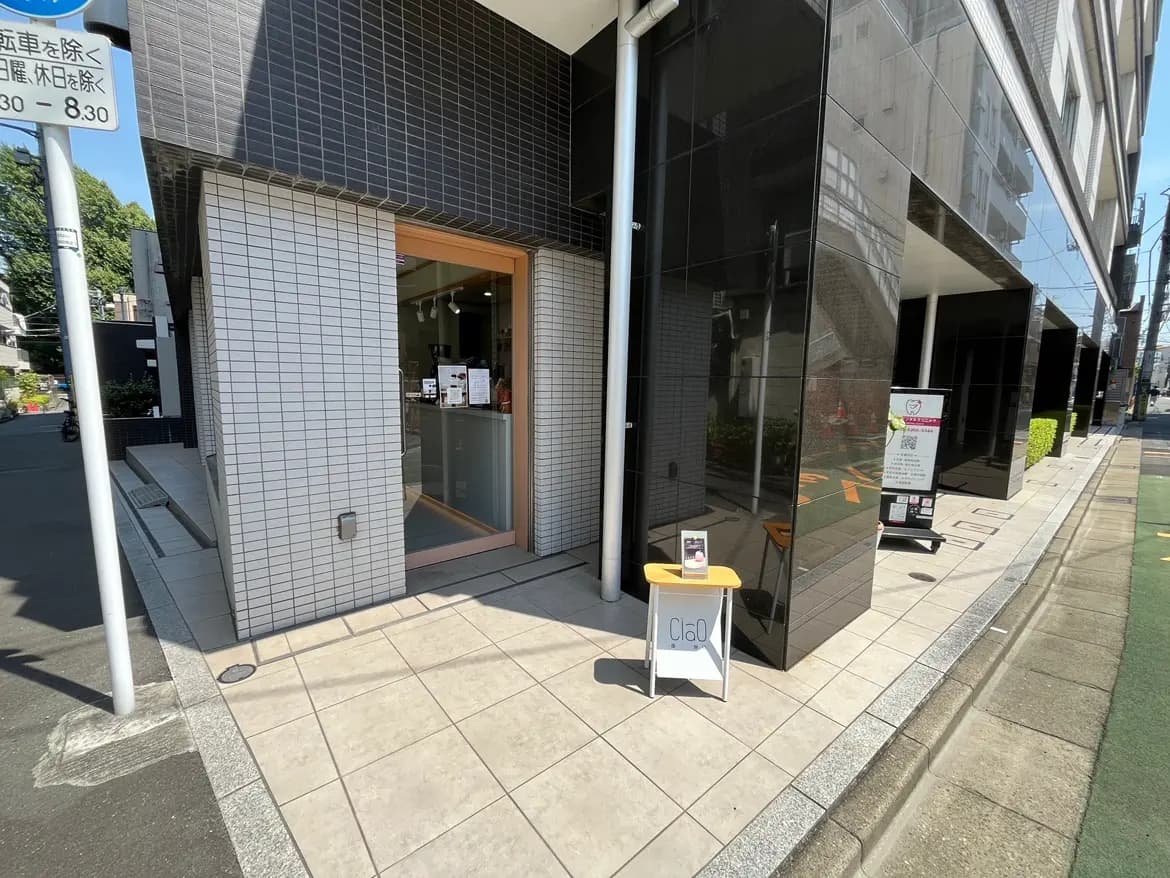 - モダンな外観の店舗入口、タイル張りの壁と透明なガラス扉、看板や案内板が並ぶ通りの風景
