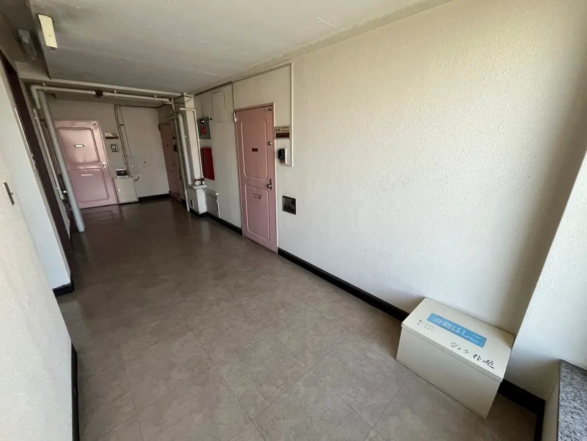 - ピンクのドアが並ぶマンションの廊下、明るい照明とシンプルな内装の壁が特徴の空間