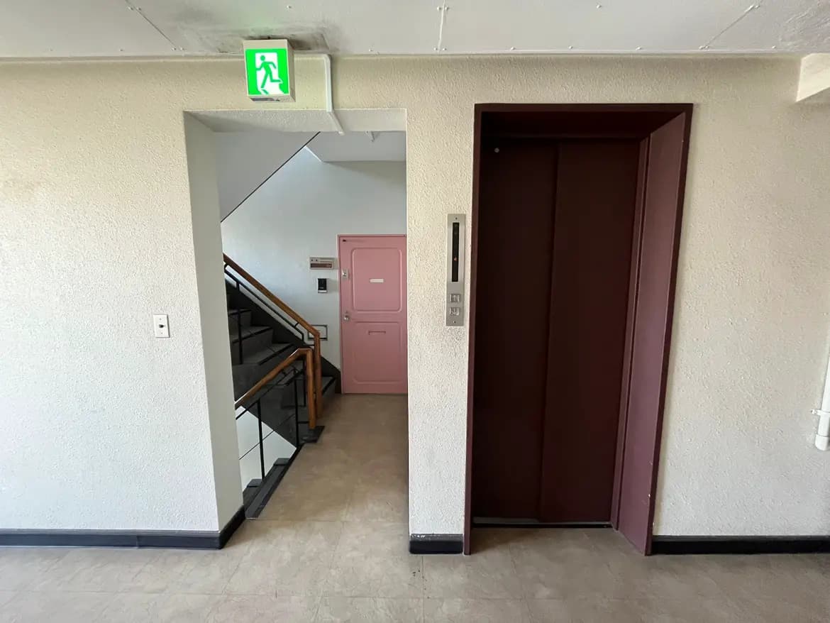 - 階段とエレベーターのある建物のエントランス、壁に緑色の避難誘導サインが表示された明るい廊下の風景
