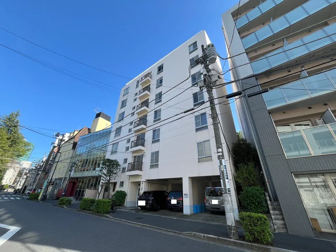 - 都市部に位置する近代的なアパートメントビル、周囲に影を落とす緑豊かな植栽と青空が広がる街並み