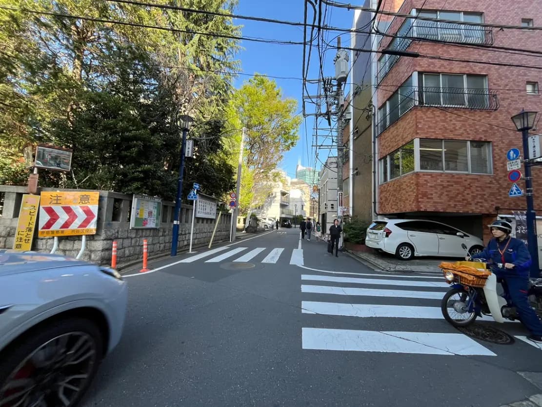 - 都市の交差点、無人の歩道と車両が通過する道路、周囲に緑が見える街並みの風景