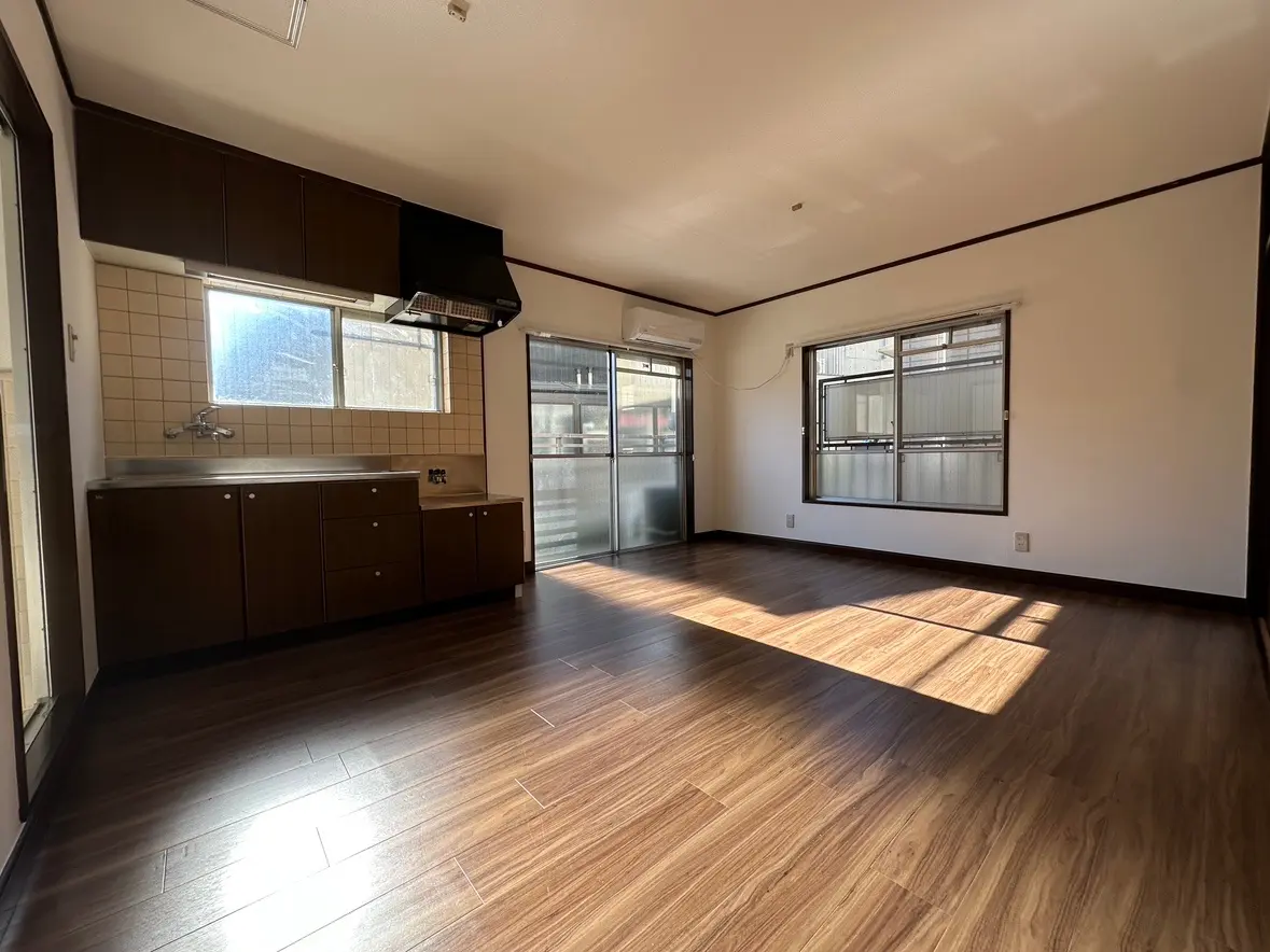 明るい自然光が差し込む広々としたキッチン、茶色のキャビネット、木目調のフローリング