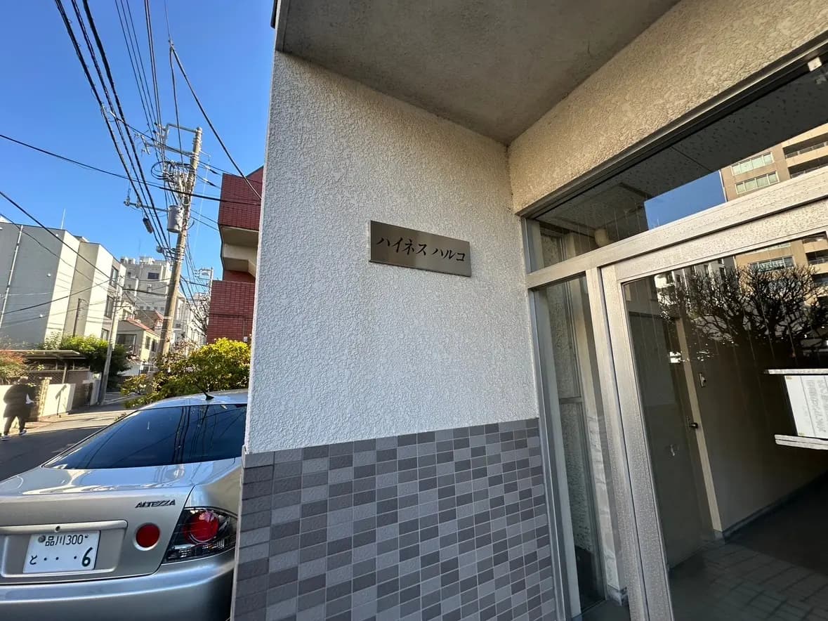 都市のアパートエントランス、タイル張りの壁とガラス扉、クリアな青空と電信柱