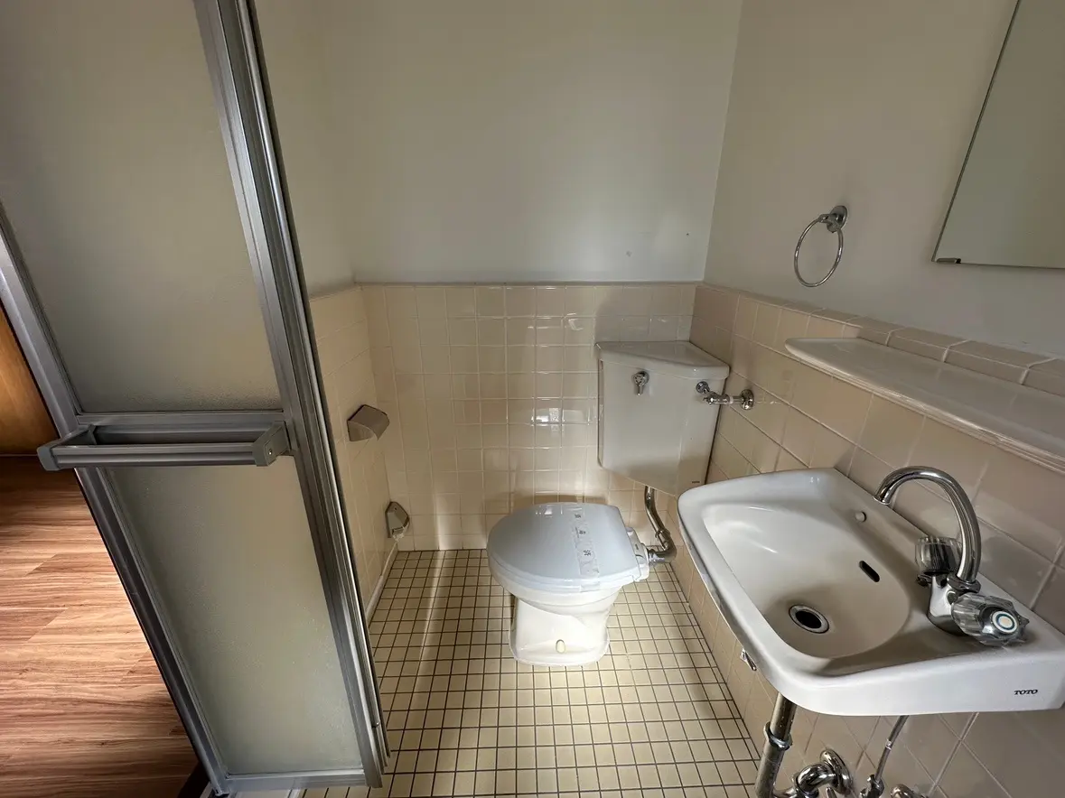 シンプルなデザインのバスルーム、タイルの壁と床、シャワー室のガラス扉、洗面台とトイレが備わったインテリア