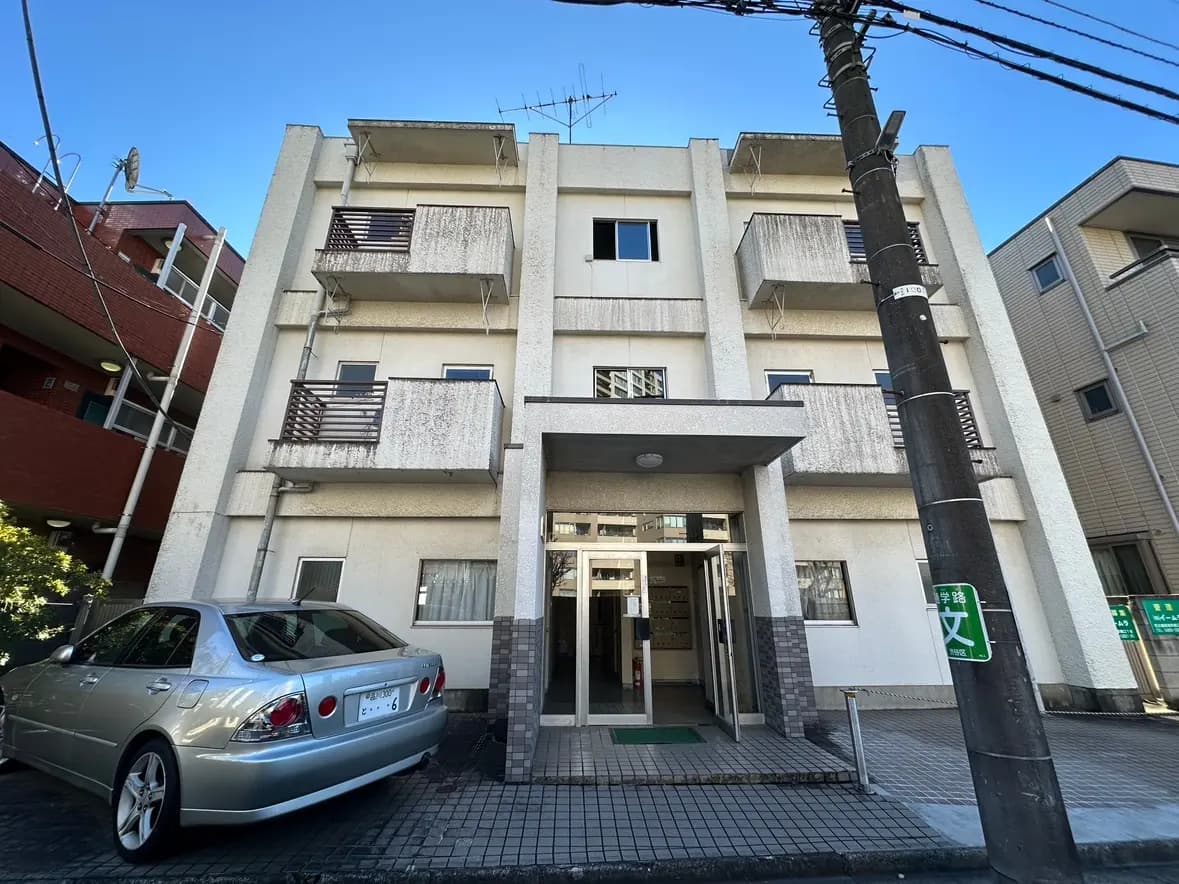 日本の都市部にある平凡なアパートの外観、駐車された車と入り口が見える