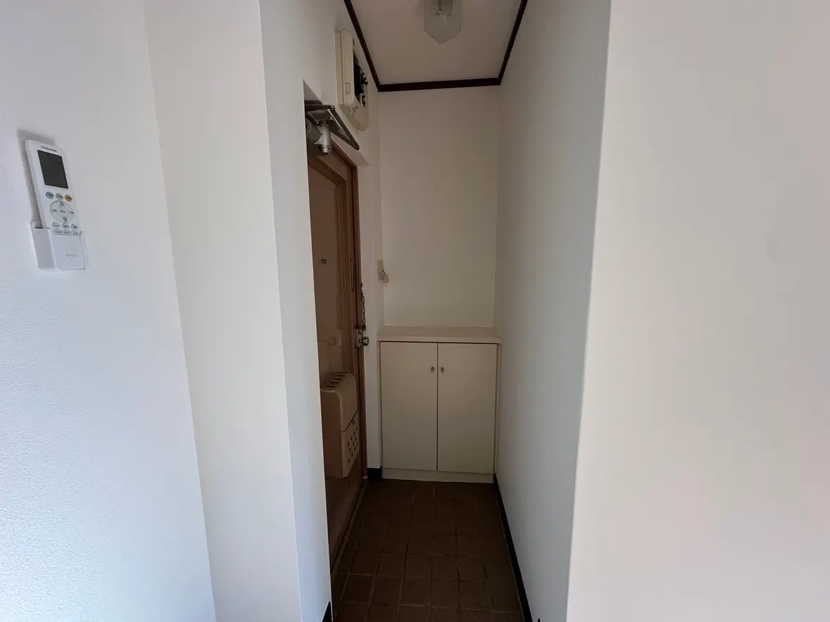 玄関の内部、白い壁とタイルのフロア、エアコンのリモコンが壁に取り付けられたシンプルなデザイン