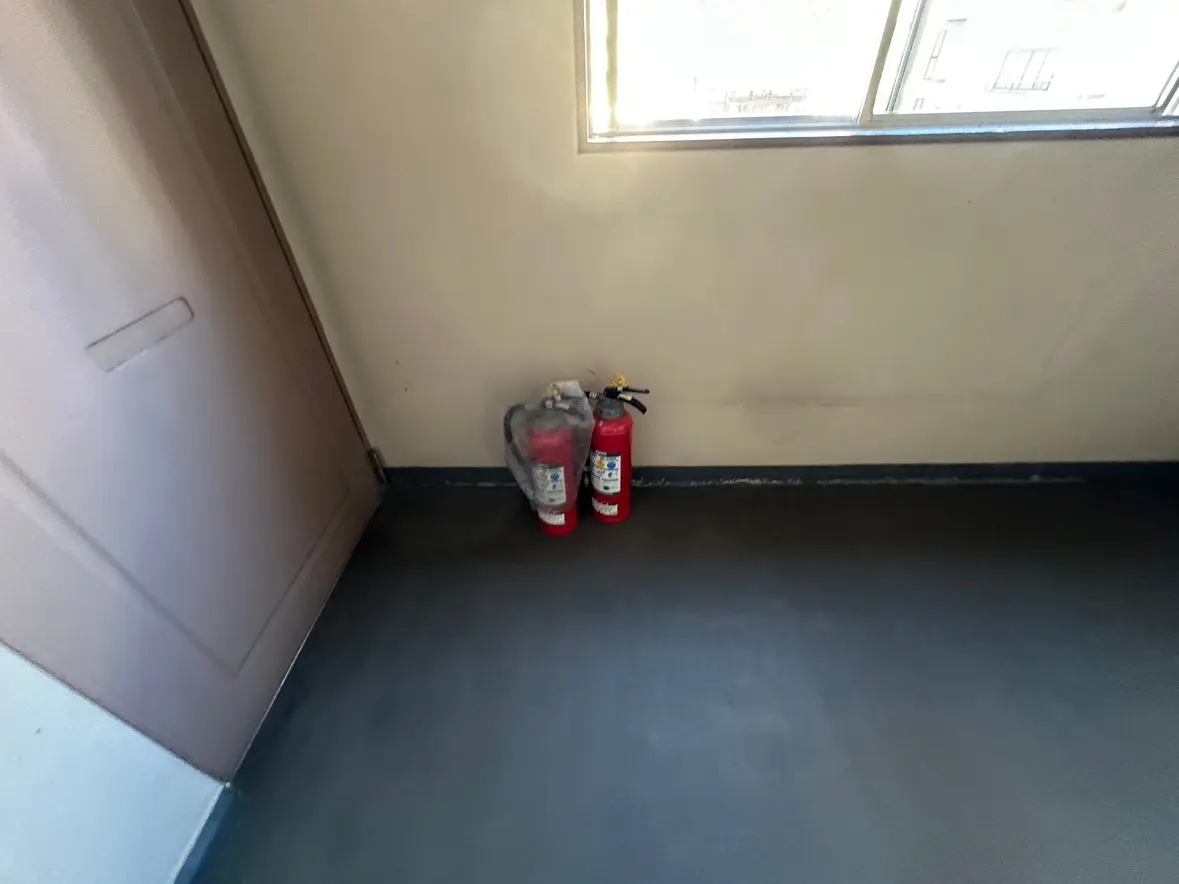 消火器が壁際に置かれているオフィスの一角、小窓から自然光が差し込むシンプルな室内