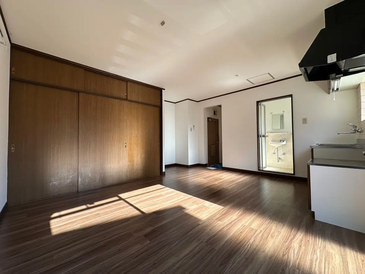 明るい日差しが差し込む空の部屋、茶色のフローリング、大きなクローゼット、そしてキッチン付きのシンプルなインテリアデザイン