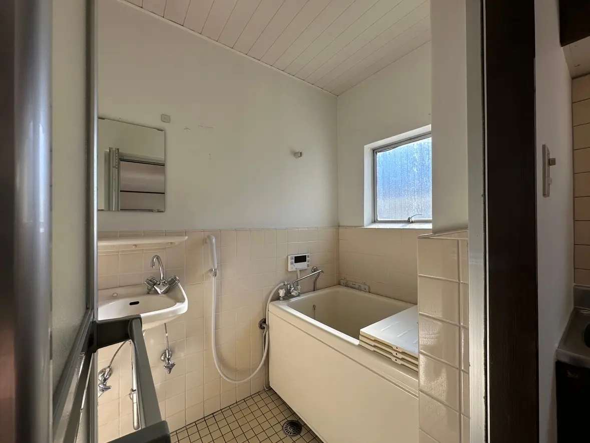 狭いスペースの洗面所とバスタブ、小窓からの自然光が明るい清潔感のあるバスルーム