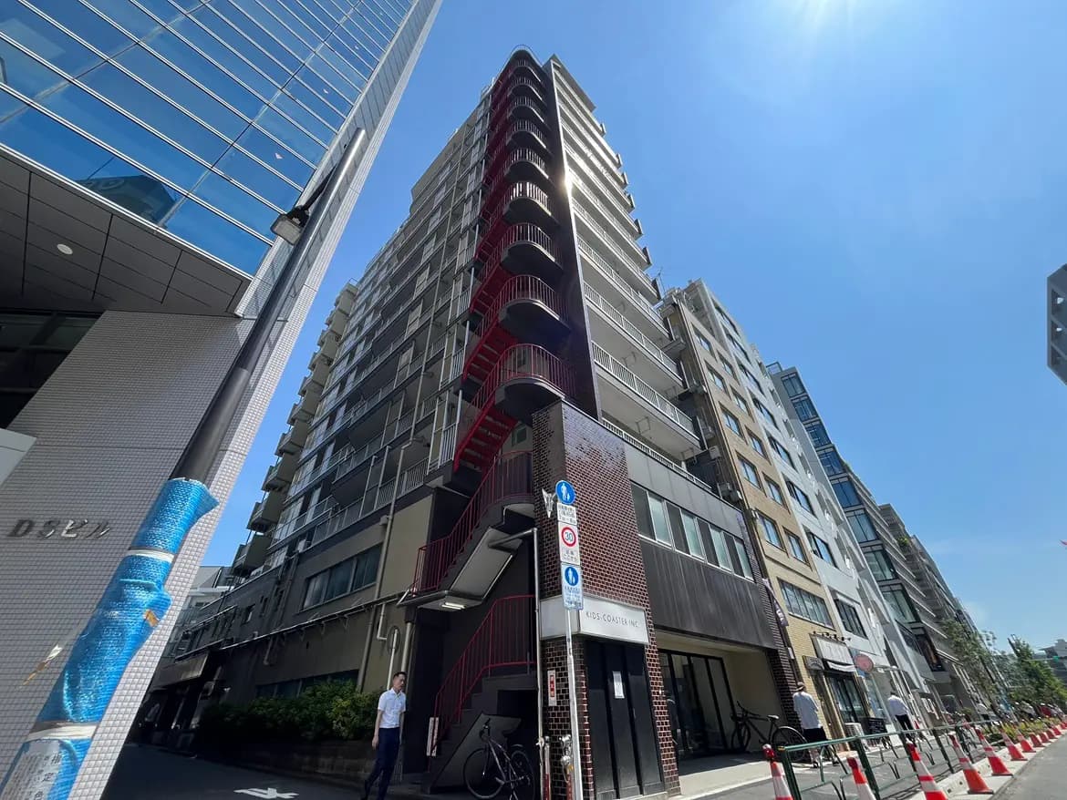 - 都市の高層ビル群を見上げる視点、赤い階段が印象的な建物と青空のコントラストが美しい風景