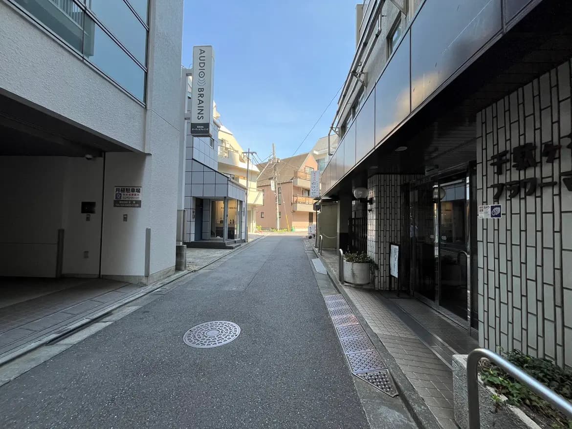 - 都会の路地、両側に建物が並び、奥に「AUDIO BRAINS」と書かれた看板が見える風景