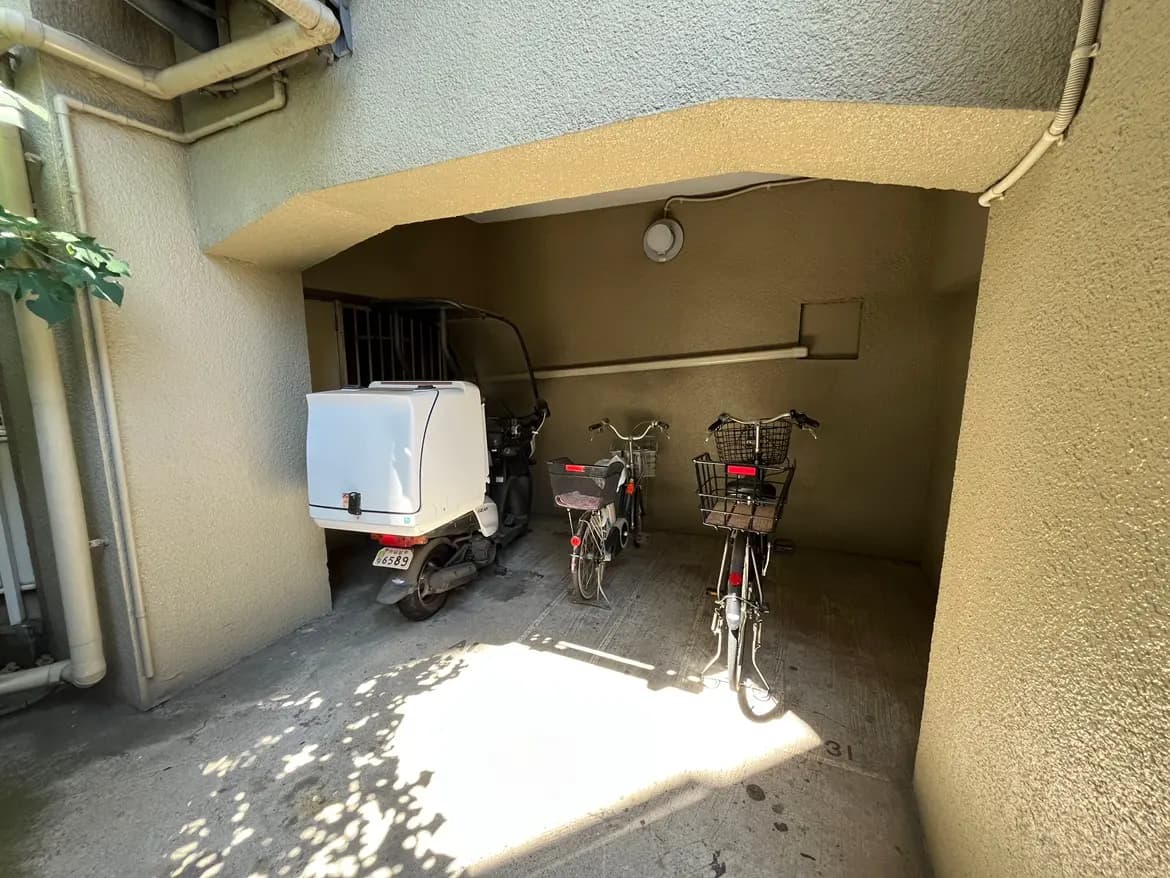 - 明るいガレージに停められたバイクと自転車、壁に囲まれたスペースで影を落とす様子