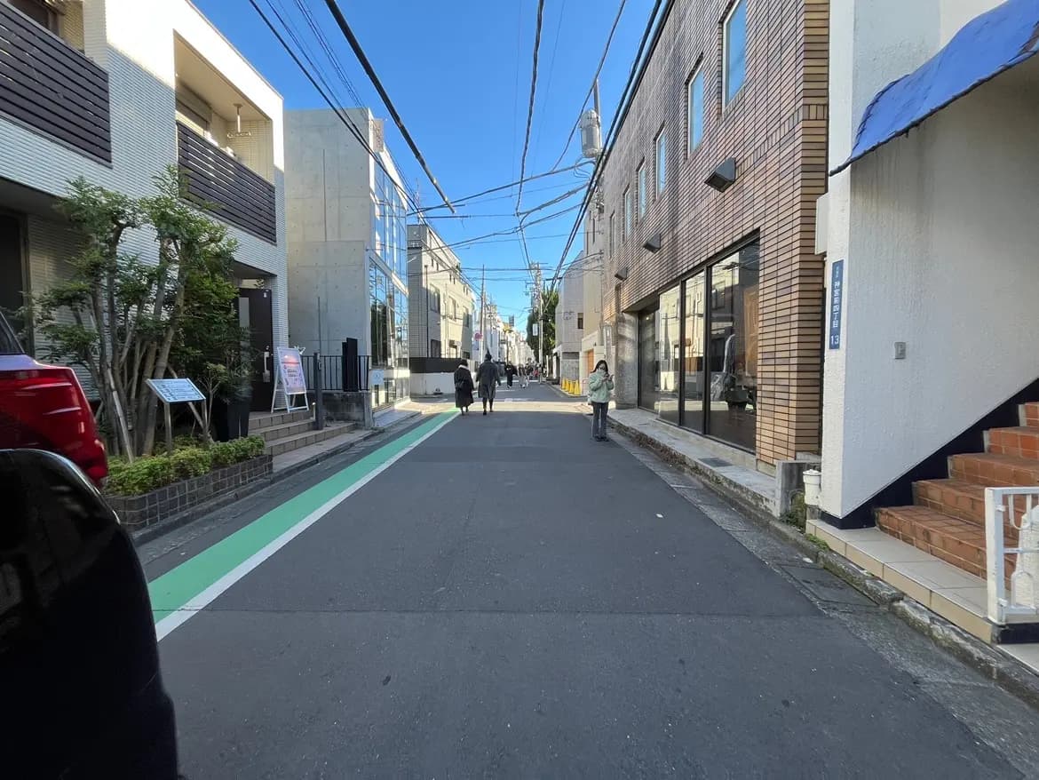 晴れた日の都市部の狭い通り、歩行者が行き交う風景、近代的な建物と店舗のファサード