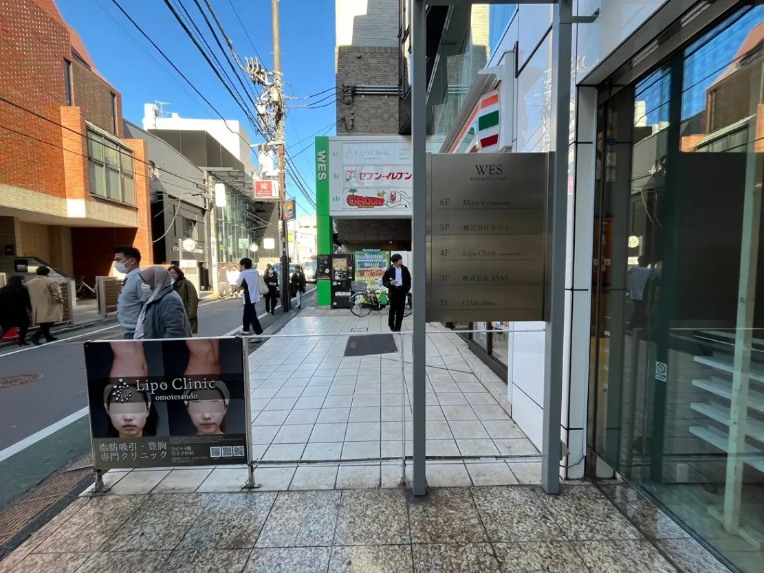 快晴の日の都市風景、ビル沿いの歩道、案内看板、多様な店舗が並ぶストリートビュー