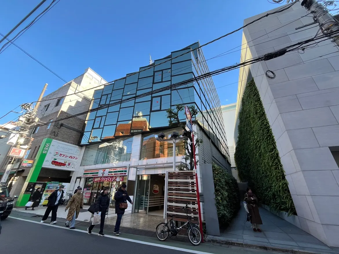青空の下、ガラス張りのモダンな建築物と歩行者、都市風景
