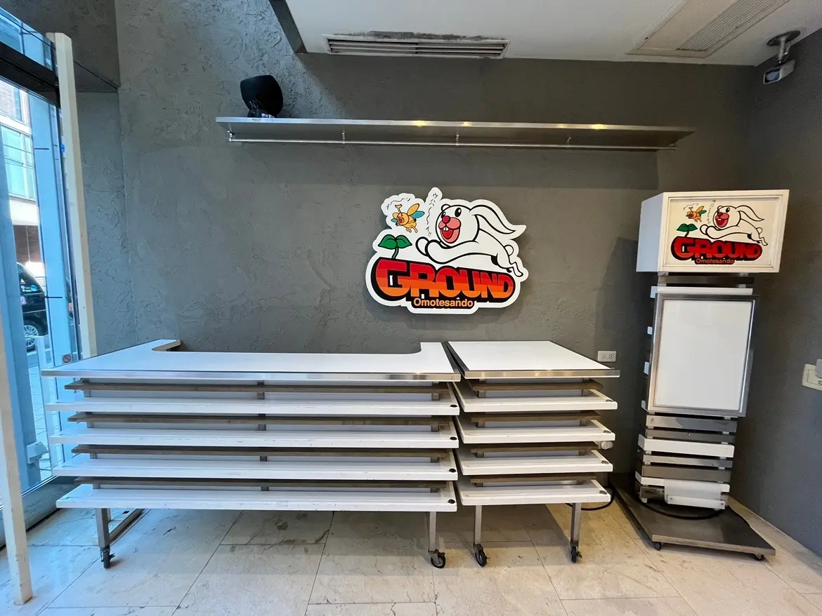 モダンな店舗の内装、積み重ねられた白い棚とロゴ入りの装飾が特徴的な壁, 看板と冷蔵庫が見える