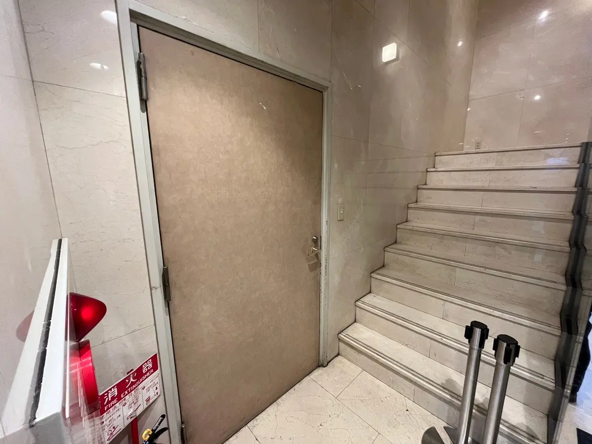 非常口の標識がある白い壁と大理石調の階段が特徴の建物内部の通路