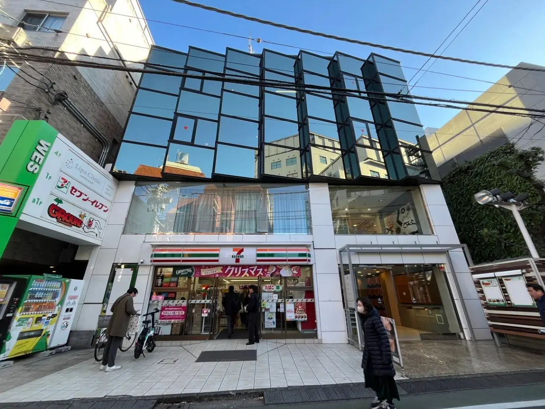 都市のコンビニエンスストアの入り口、現代的な建物のファサード、歩行者と自転車が見えるストリートビュー
