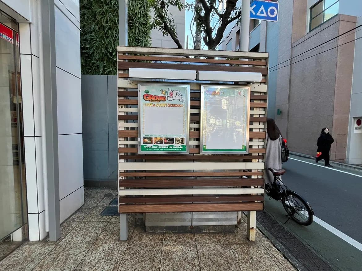 市街地にある屋外の掲示板、木製のベンチ、通りを歩く人々