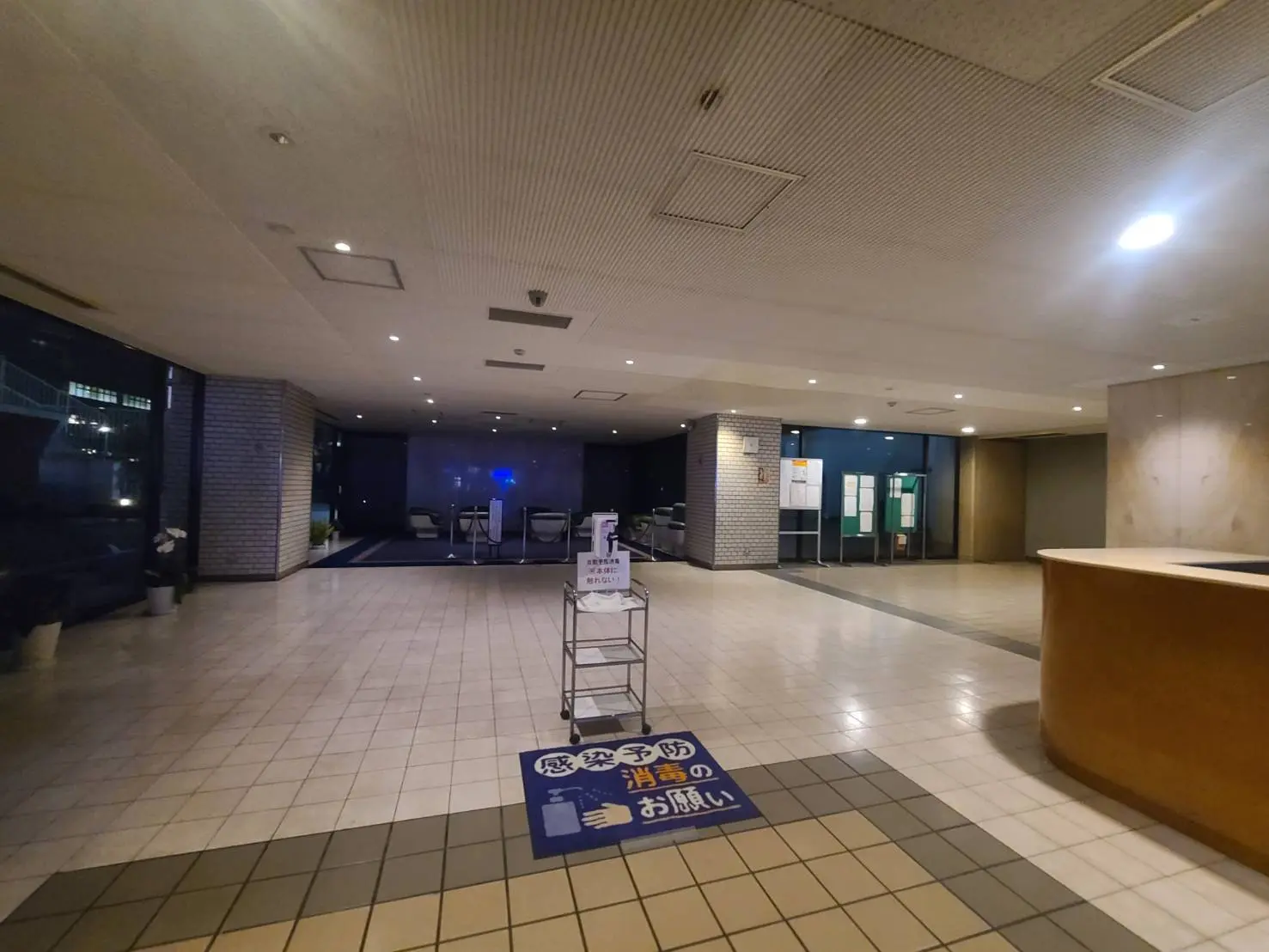夜間照明のある静かなオフィスビルのエントランスロビー、床はタイル貼りで受付カウンターと案内板が見える