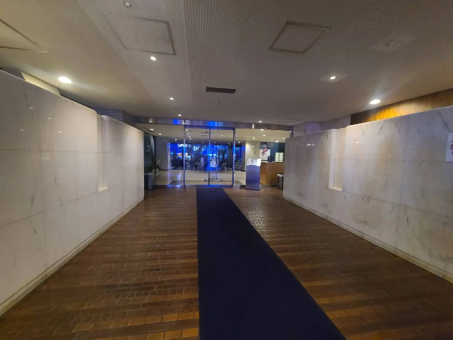 ビジネスビルのエントランスホール、大理石の壁面、木目調の床、吹き抜けの天井デザイン