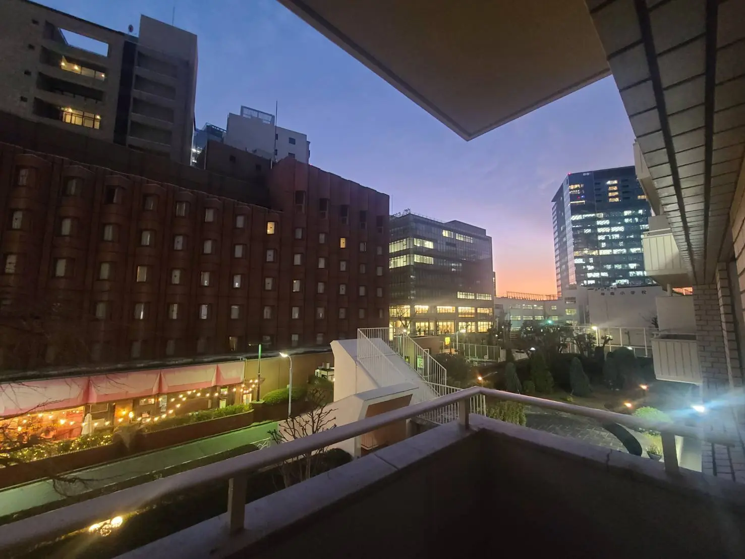 夕暮れ時の都市風景、ビル群にオレンジ色の空、ライトアップされたレストランと居住区