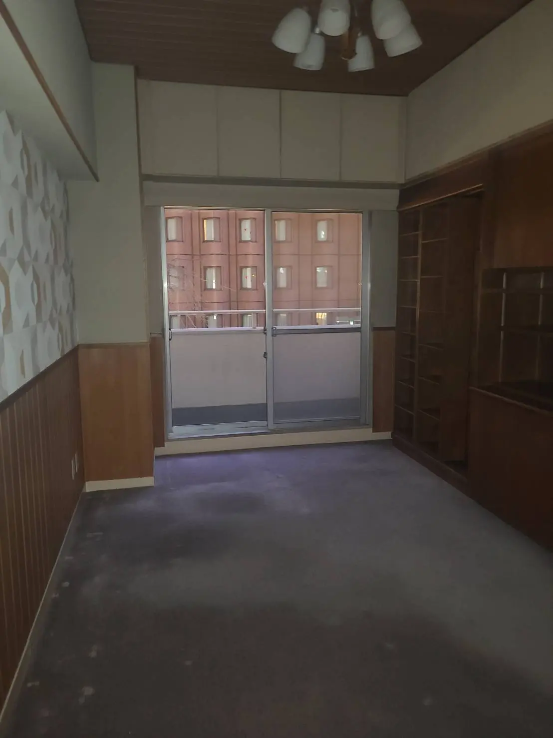 レトロなデザインの空の部屋、木目調の壁と天井、床にカーペット、バルコニー付きの大きな掃き出し窓