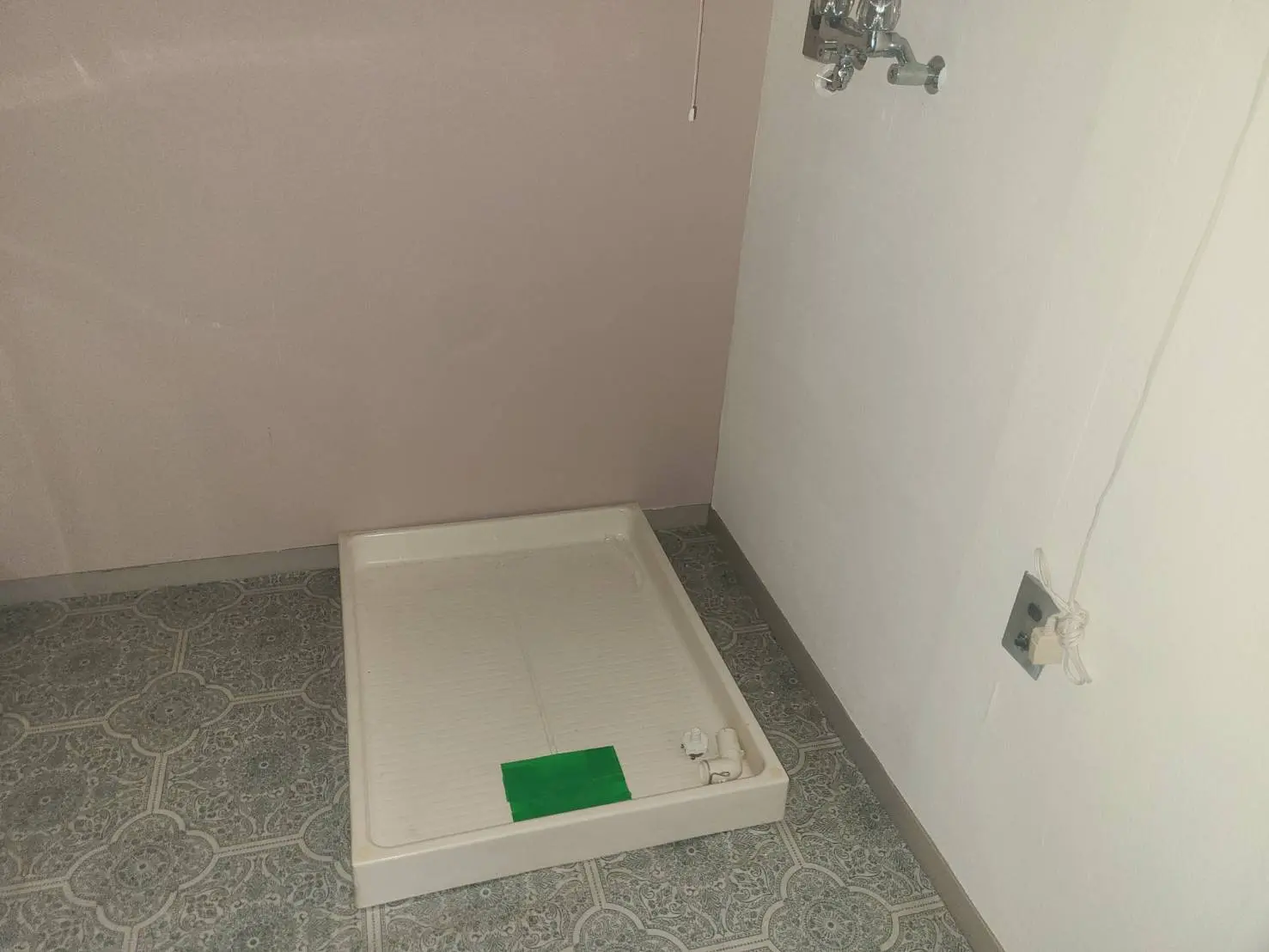 改装前の空の部屋、古い模様のフローリング、壁に取り付けられたシャワー設備